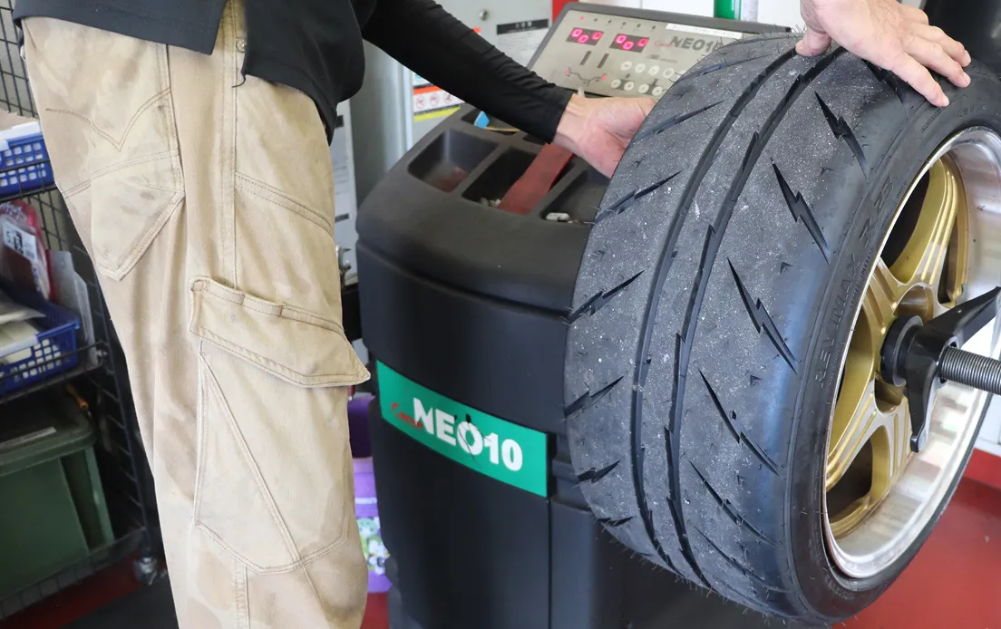 サーキット走行前に、ホイールバランサーでタイヤのバランスを最終確認し、レーストラックで車両性能をテストしている複合的な様子。